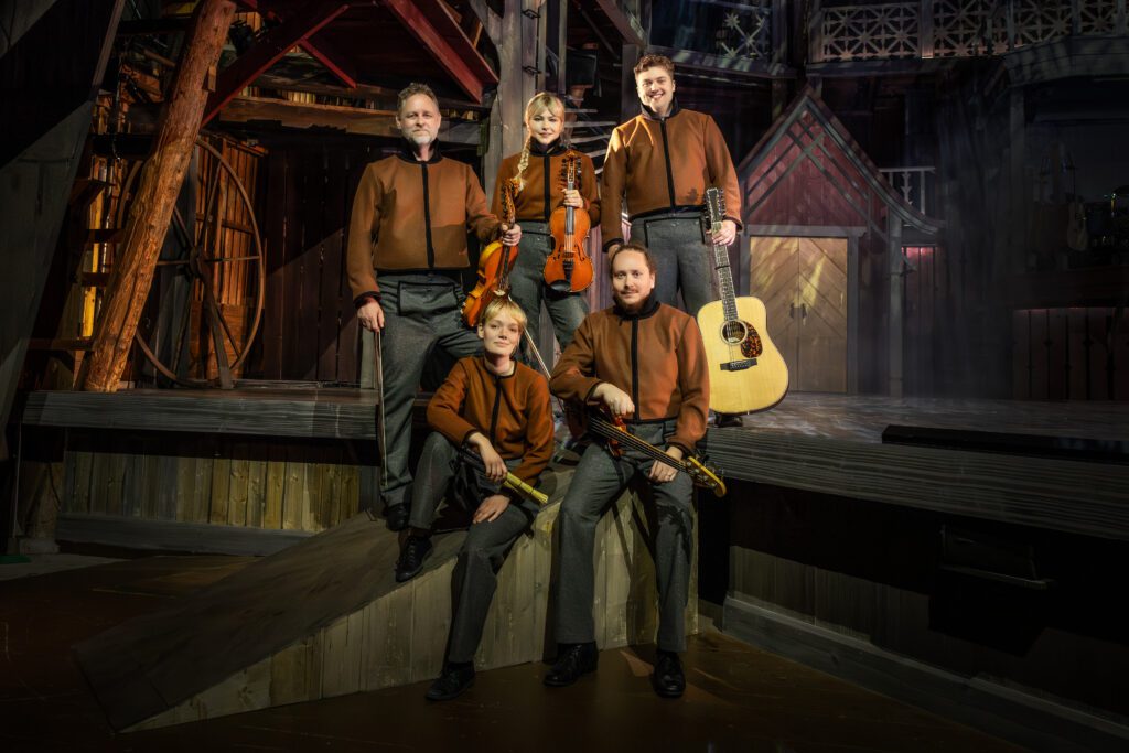 Fem orkestermusiker sitter och står på scenkanten med instrument i händerna