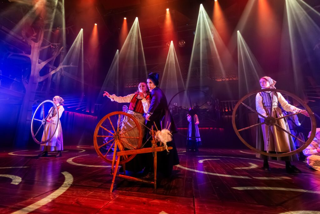 Scenbild från Liljecronas hem med pigor som håller i stora trähjul som ska symbolisera spinnrockar.