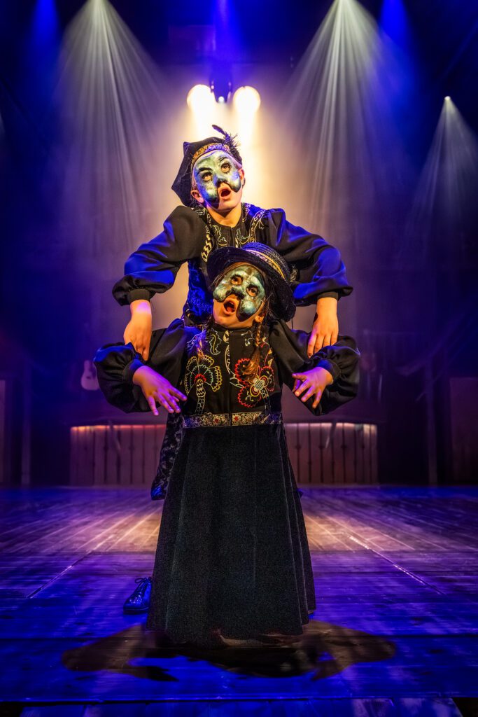 Scenbild från Liljecronas hem där två barnskådespelare med masker och mörka kläder spelar två dansande vättar.